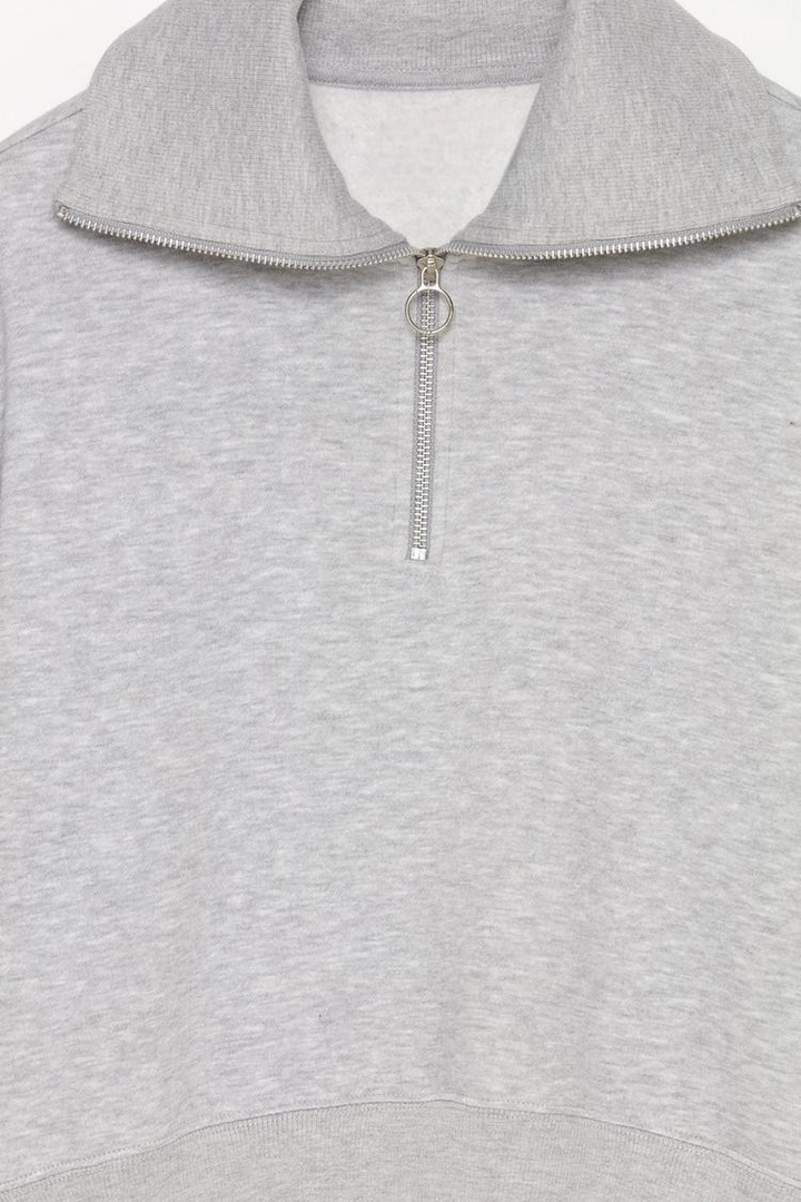 Zoomed-in view of a women's grey sweatshirt with a zip-up collar, highlighting the fabric texture, zipper details, and stitching.