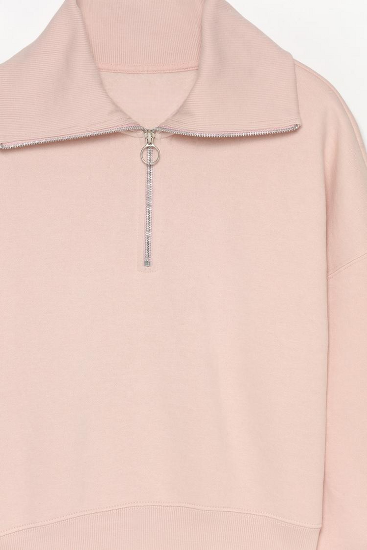 Zoomed-in view of a women's pink sweatshirt with a zip-up collar, highlighting the fabric texture, zipper details, and stitching.