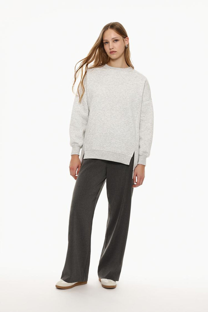 Zoomed-in full-body view of a women's grey oversized sweatshirt, showcasing the asymmetric design and relaxed fit with close-up details of the fabric.