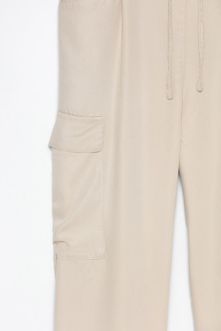 Detailed product image of the beige flowing cargo joggers, emphasizing their texture and functional design.