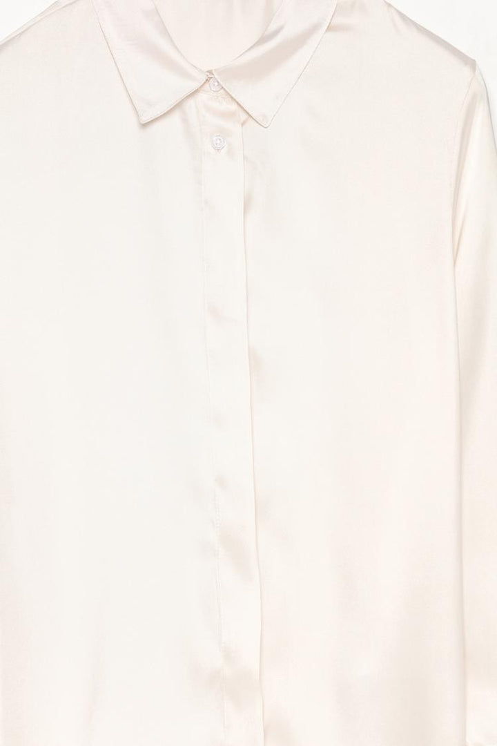 A close-up image of a white long-sleeve satin shirt, focusing on the smooth, glossy fabric and the intricate details of the button-down front and classic collar. The zoomed-in view highlights the luxurious texture and craftsmanship.