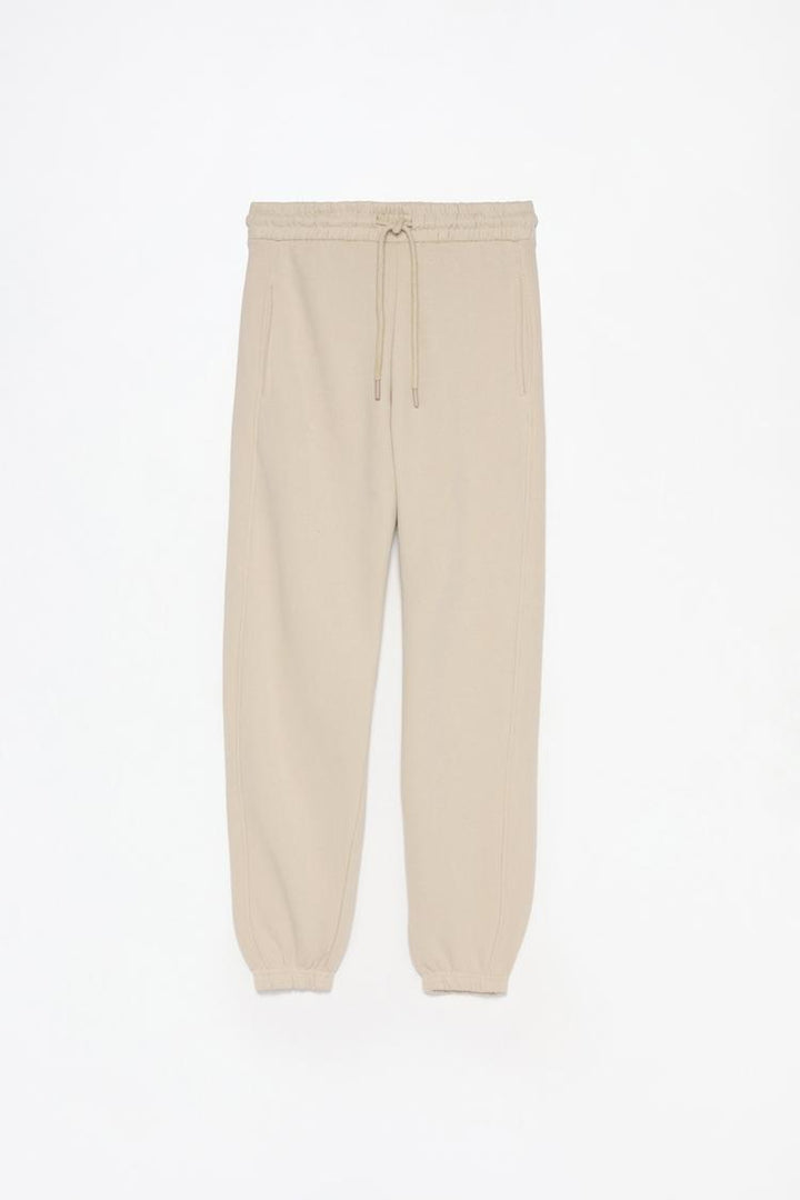 Full product shot of the beige oversized tracksuit trousers, showing all design elements and fabric details.