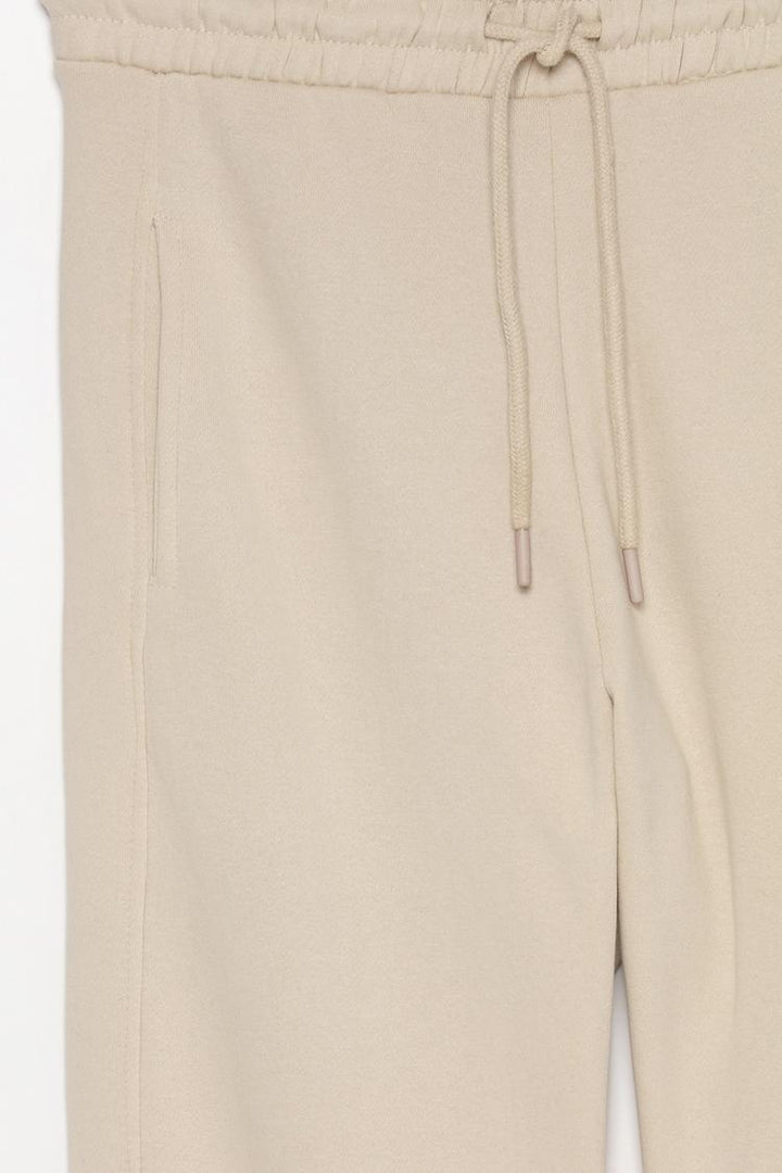 Detailed close-up image of the beige oversized tracksuit trousers, focusing on fabric texture and stitching.