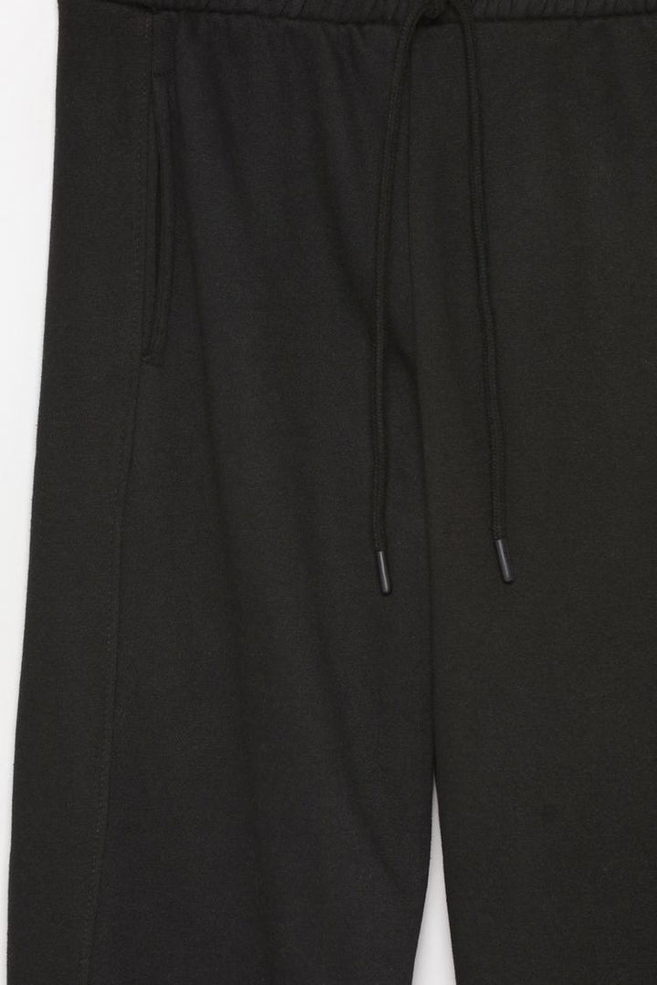 Close-up of the black oversized tracksuit trousers, highlighting fabric details and overall design.