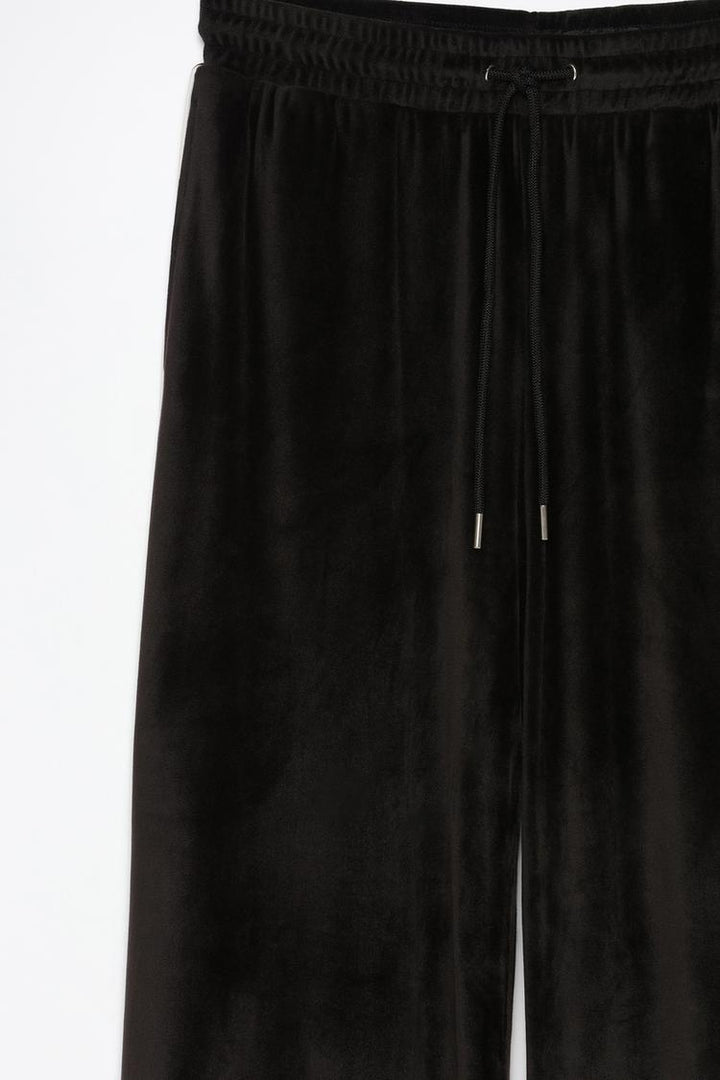 Product view of black oversized velvet trousers showing fabric details and style.
