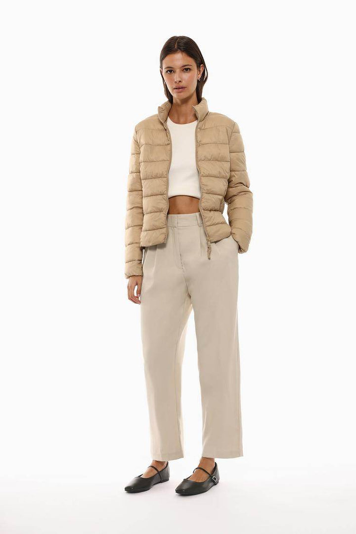 Full body front view of woman wearing beige lightweight puffer jacket

