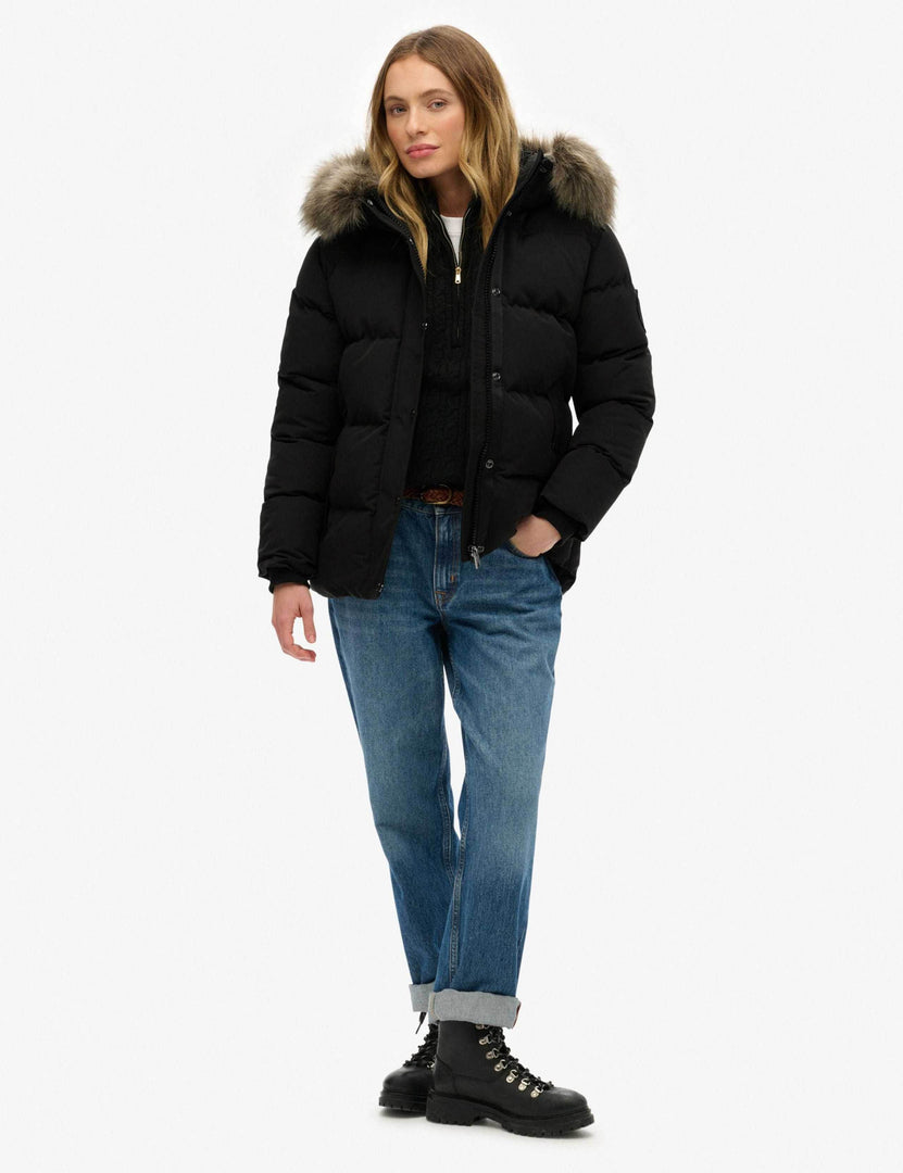 Full body front view of a woman wearing a black hooded funnel neck puffer

