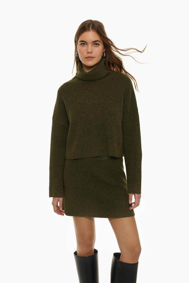 Full body front view of woman wearing dark green turtleneck sweater

