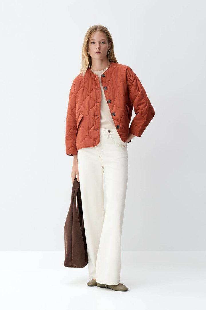 Full body front view of a woman wearing an orange quilted jacket

